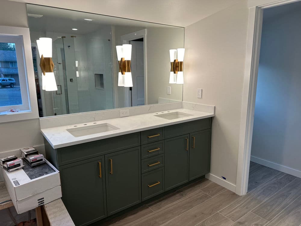 Modern bathroom with dual sinks, green cabinetry, and stylish lighting fixtures.