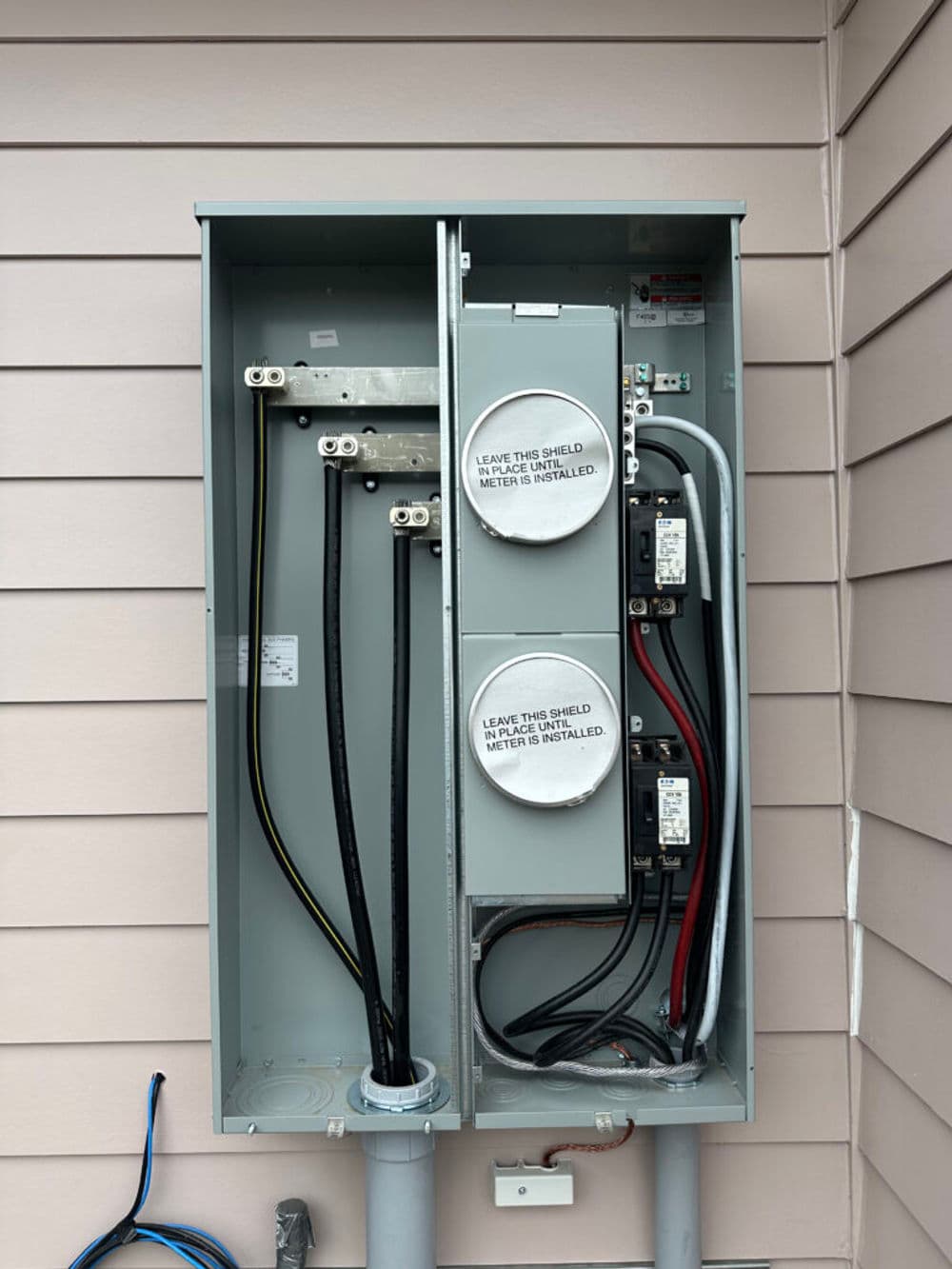 Electrical meter panel with two meters and multiple cables mounted on a house wall.