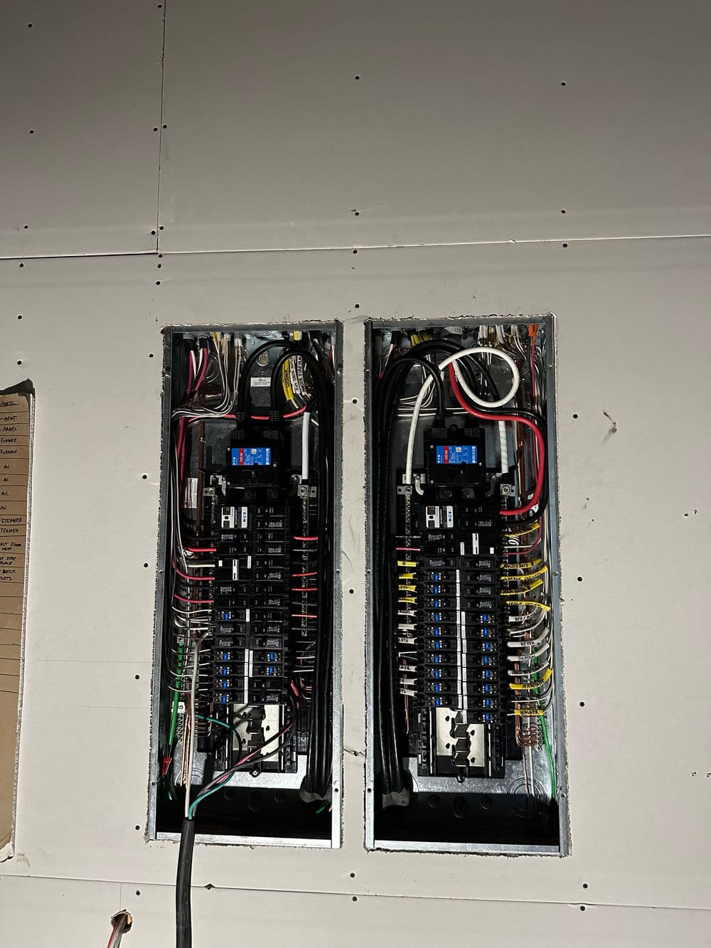 Electrical panel installation showing two circuit breaker boxes with wires and connections.