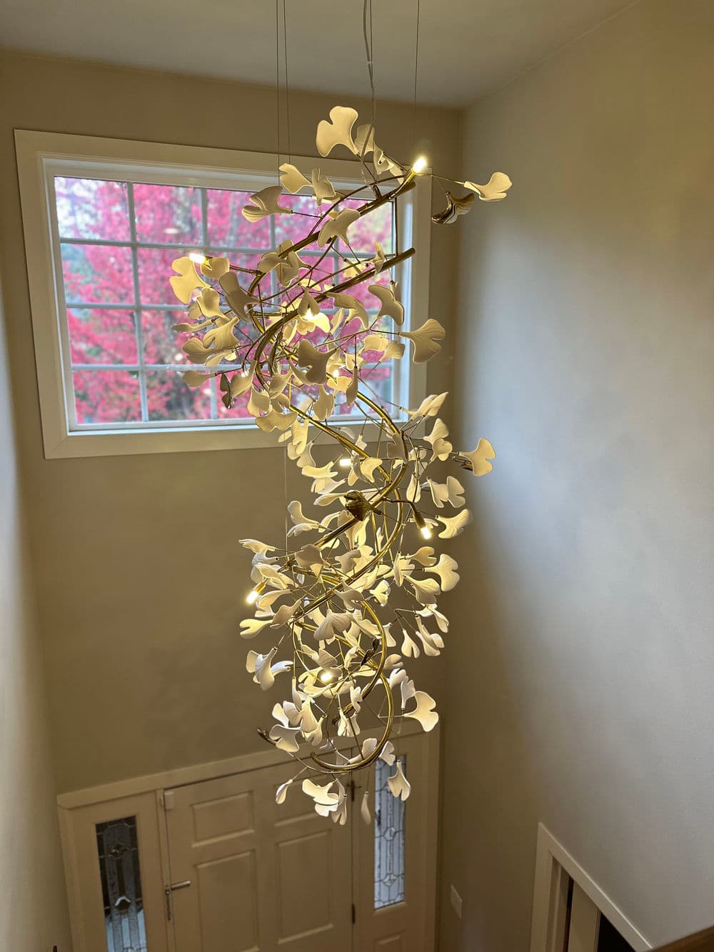 Modern pendant light fixture with white floral design, illuminating a stairwell with colorful window view.