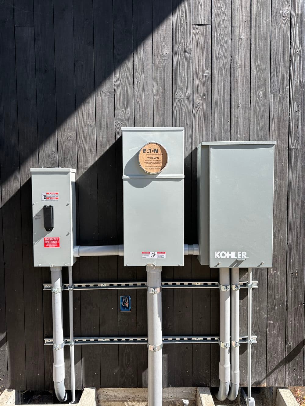 Kohler electrical panel and junction box mounted on a dark wooden wall.