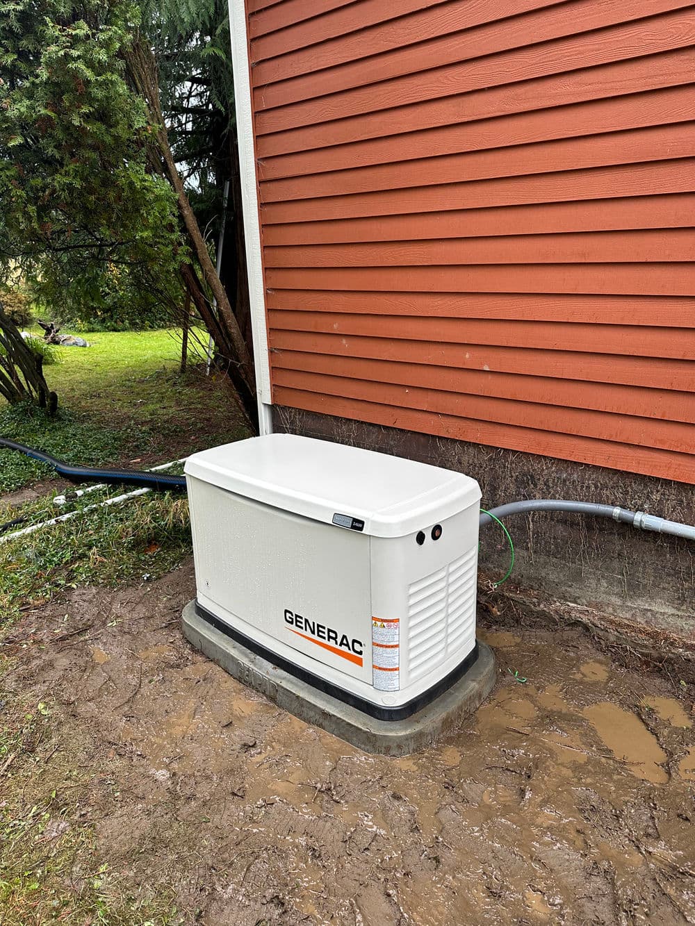 Generac generator installed outside a home next to a red wooden wall.