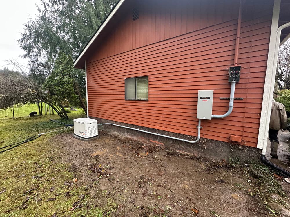 Red house exterior with electrical panel and generator in a yard surrounded by trees.