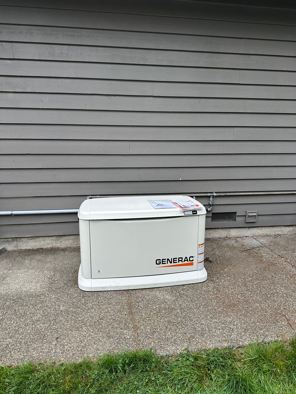 Generac standby generator installed beside a gray house, ensuring reliable power supply.