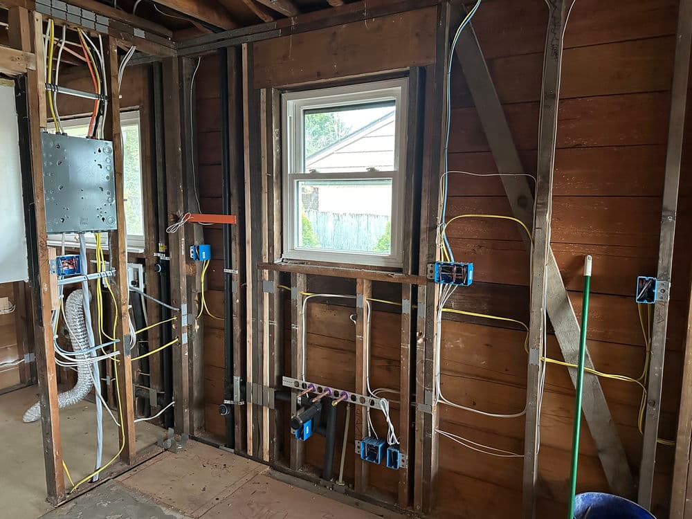 Electrical wiring installation in a home renovation project with exposed studs and window.