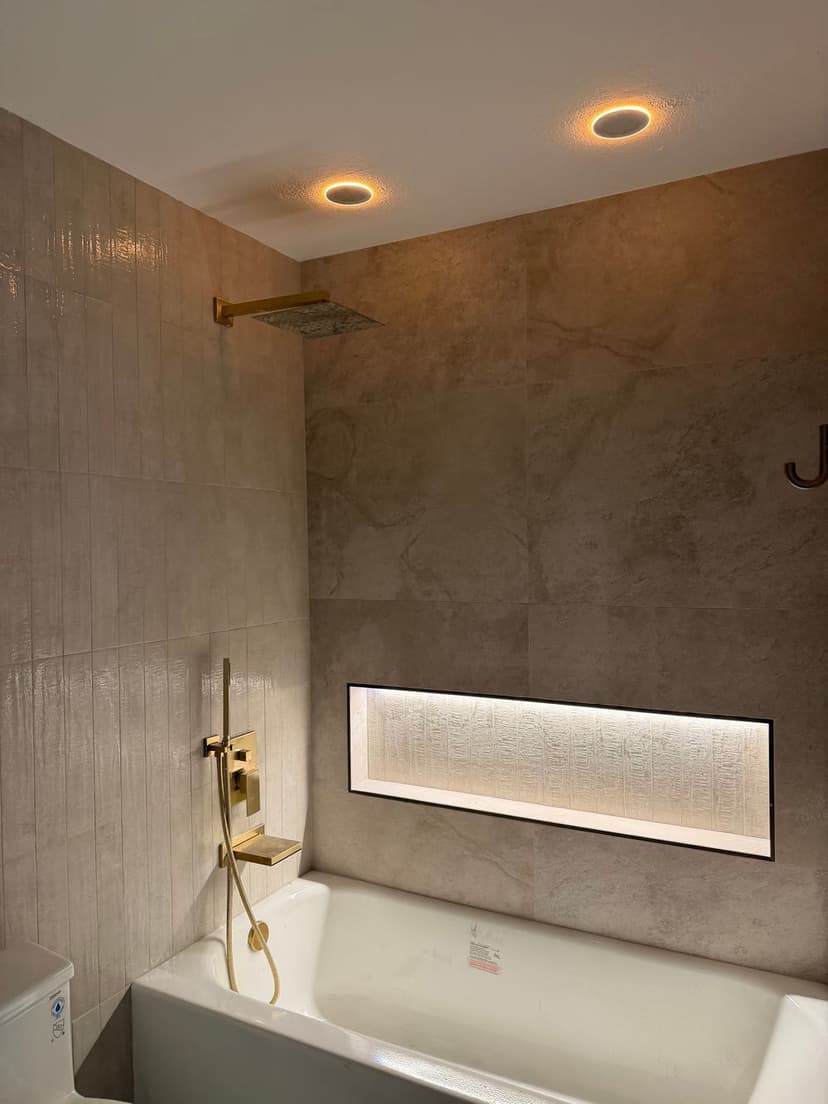 Modern bathroom featuring a sleek bathtub, gold fixtures, and recessed lighting.