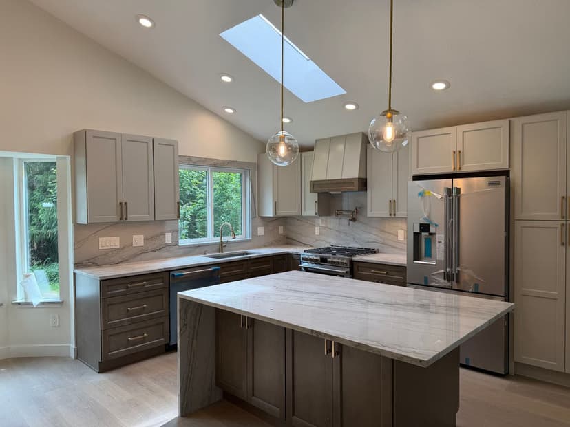 Modern kitchen with light cabinets, marble countertop, stainless steel appliances, and skylight.
